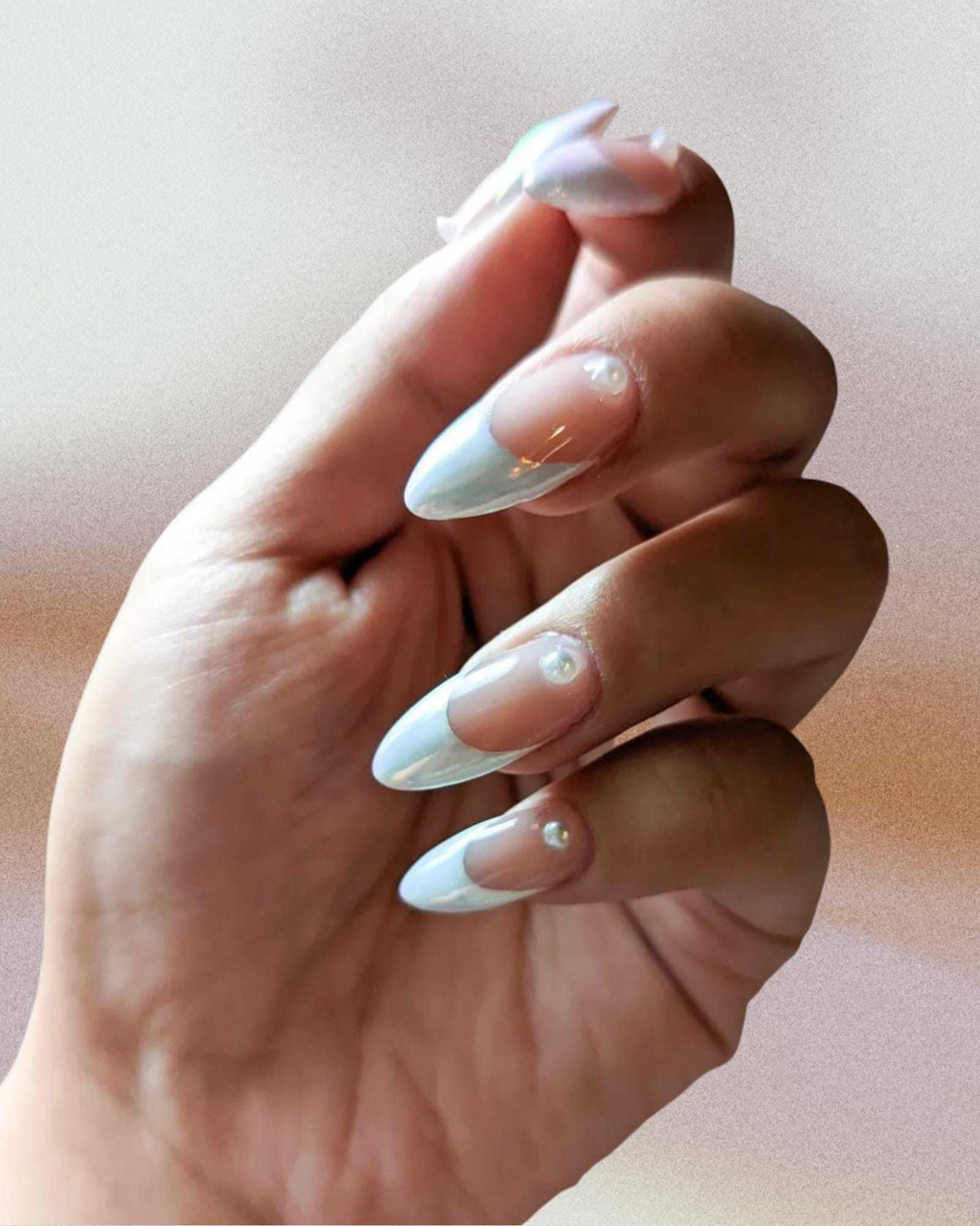 Elegant hand with pastel pink and white ombre nails with pearl accents.